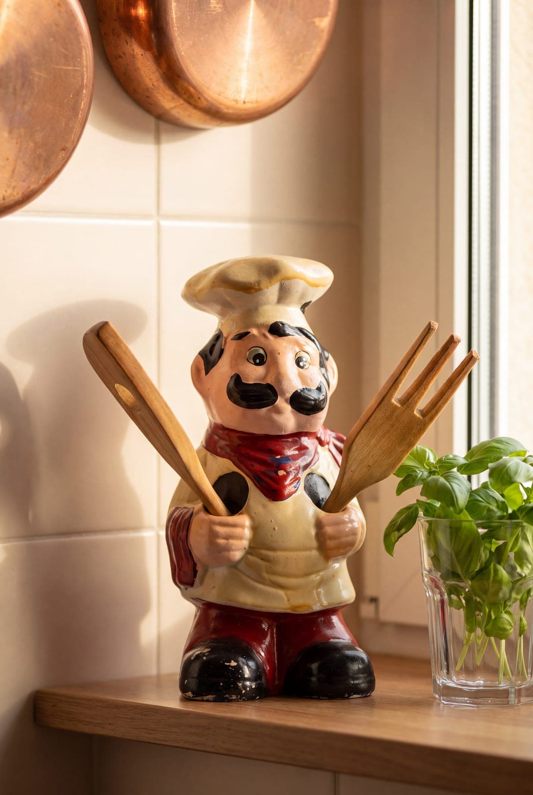Hand-painted ceramic chef figurine holding two wooden utensils on a kitchen counter. AI-generated · Nano Banana Pro