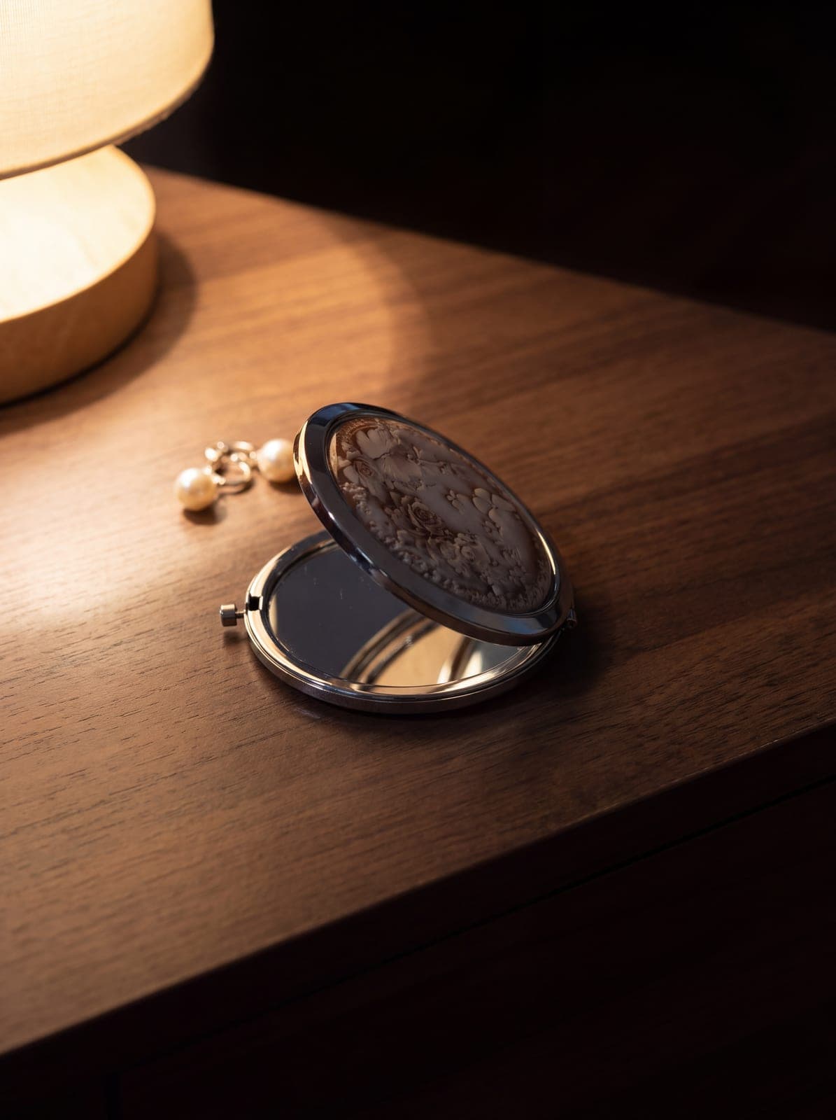 Round chrome compact mirror with a marbled rose lid, its open lid reflecting a lamp and the ceiling. AI-generated · Nano Banana Pro