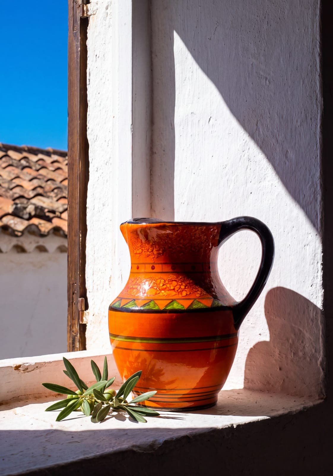 Hand-painted orange ceramic jug with green triangles and a black handle on a sunlit windowsill. AI-generated · Nano Banana Pro + Kling 3.0 Turbo
