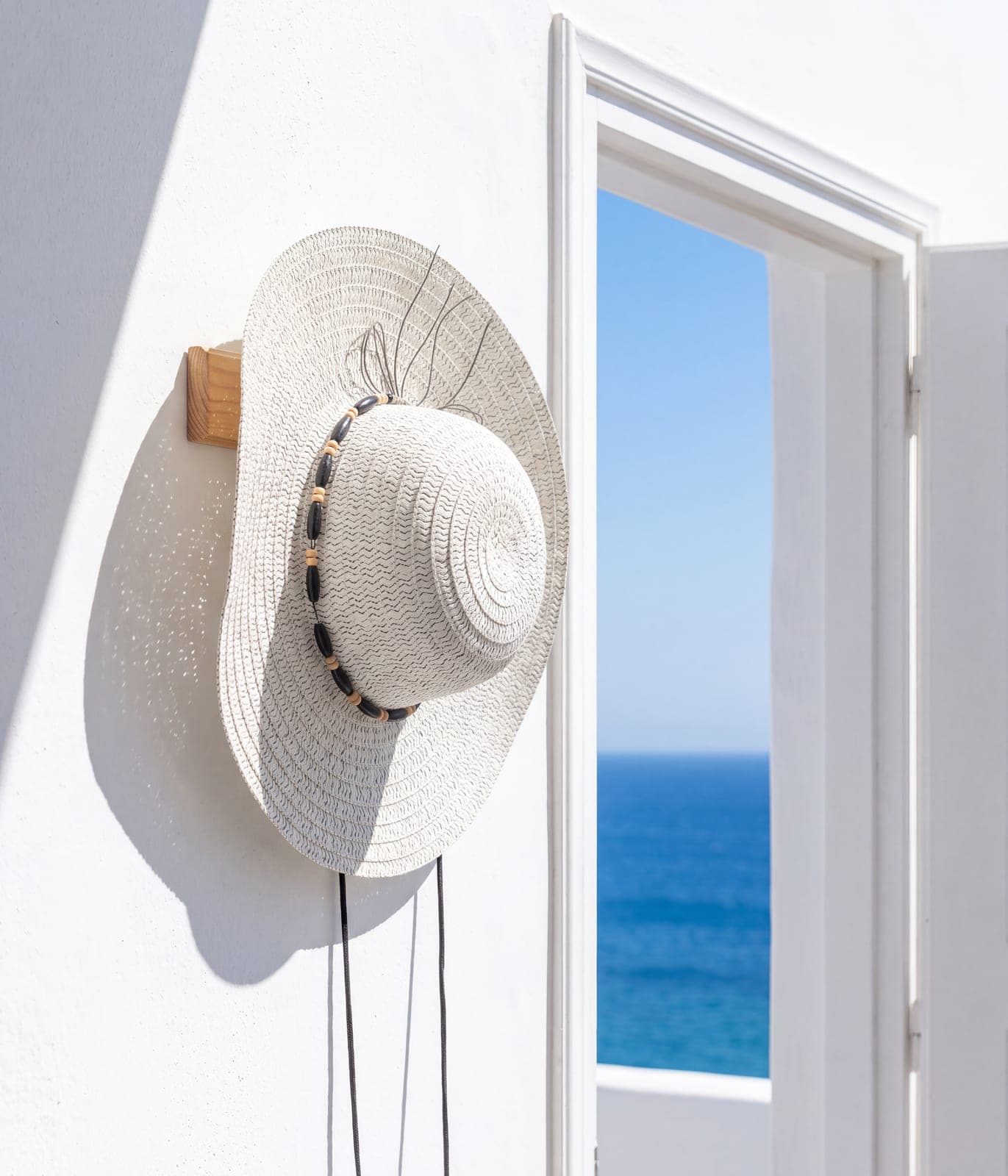 Woven straw sun hat with a beaded band hanging in a bright doorway. AI-generated · Nano Banana Pro