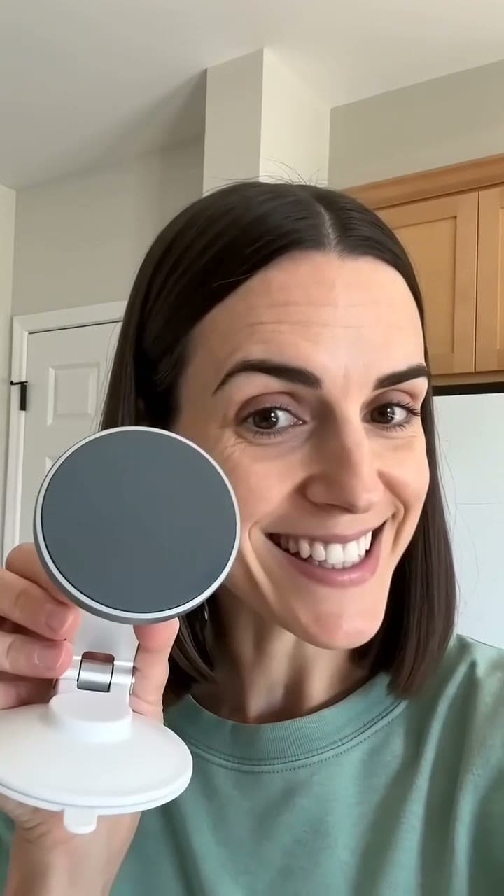 A woman holds up an unbranded phone stand in her kitchen, then presses it onto the wall tiles and clicks her phone onto it. AI-generated · Seedance 2.0